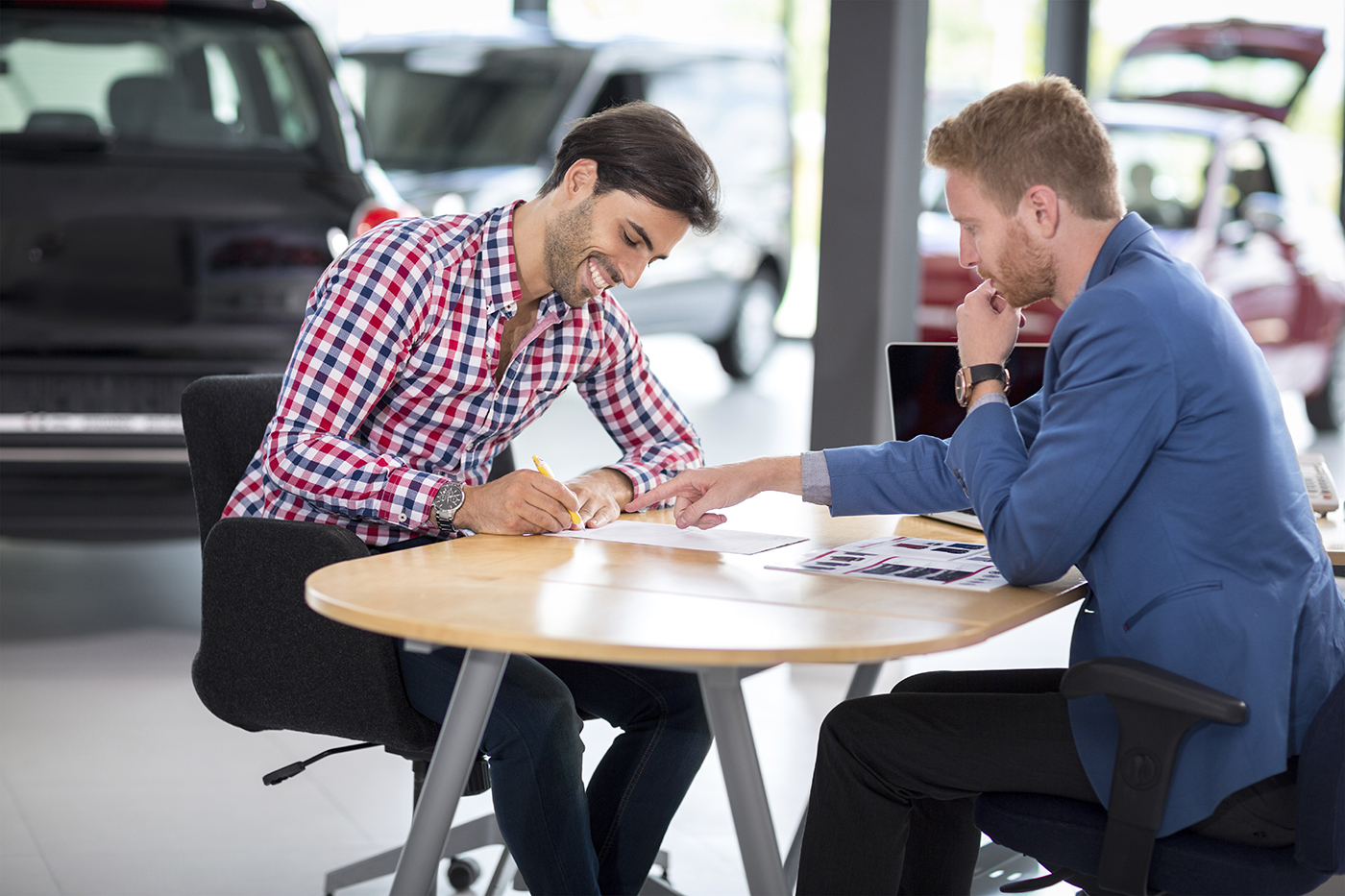 Happy man with car dealer buying a car signs the contract in car showroom